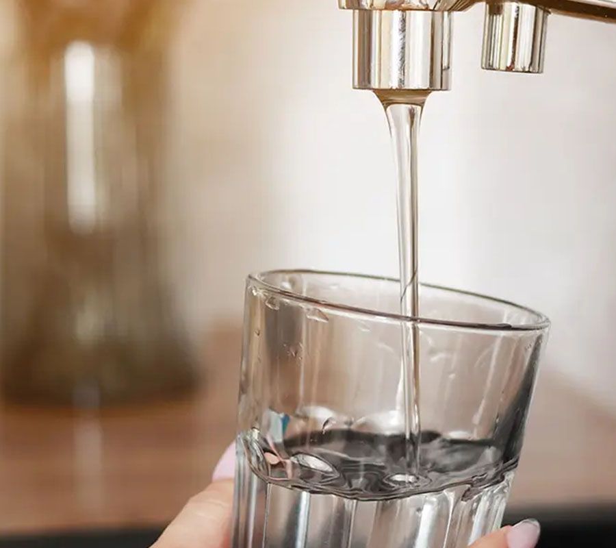 A close-up of clear water pouring from a metal faucet into a glass held by a hand.