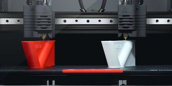 Een 3D-printer print een rode beker en een witte beker