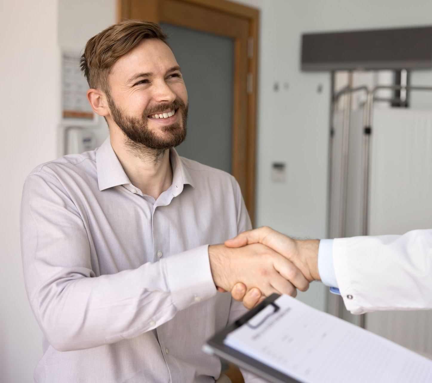 Mann schüttelt jemandem in einem weißen Kittel die Hand, lächelnd in einer medizinischen Umgebung