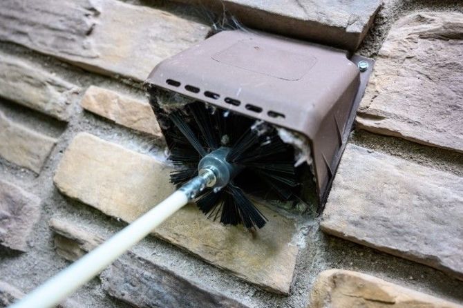 A brush is being used to clean a chimney on a brick wall.