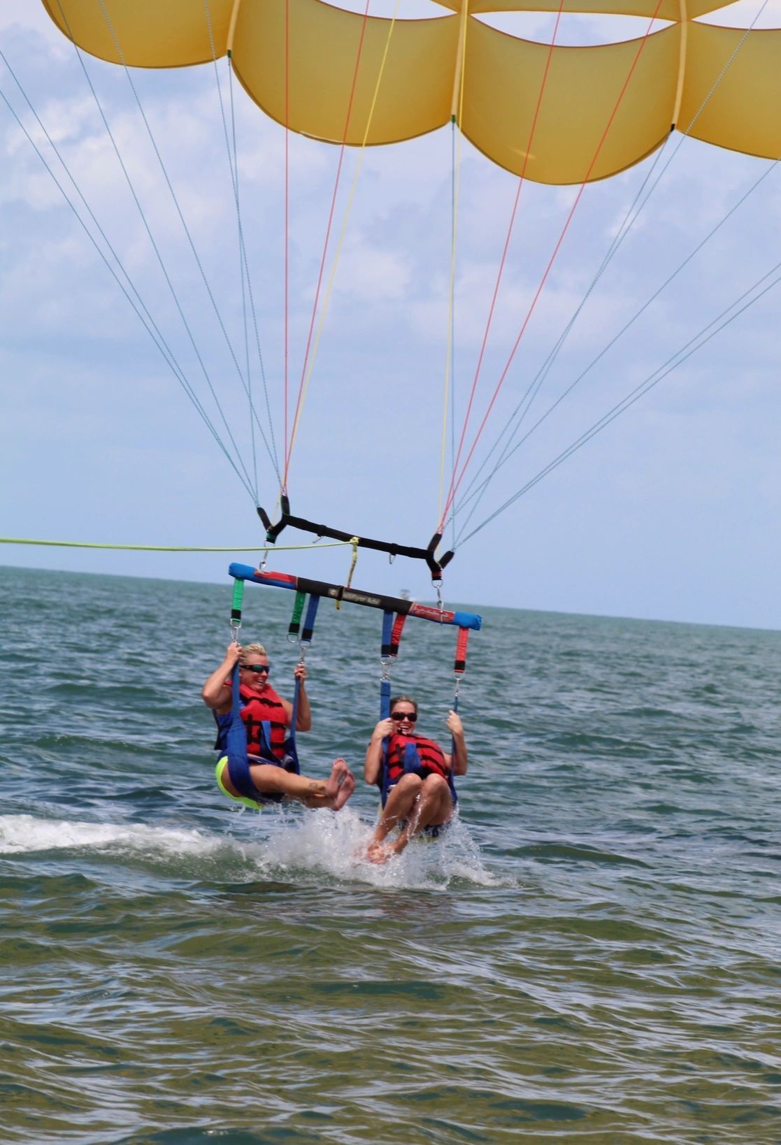 Two people are flying through the air on a parachute over the ocean.