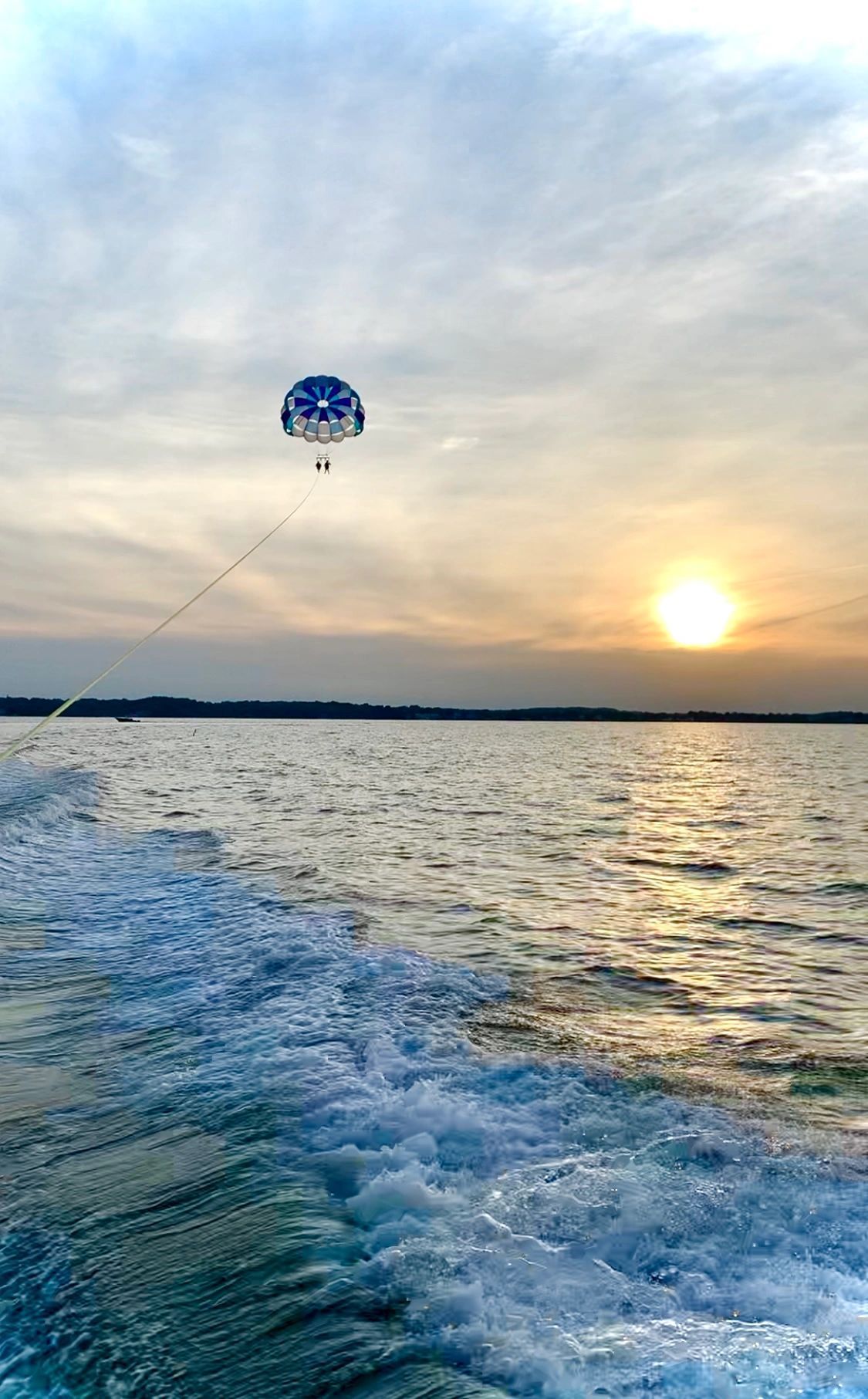 A person is parasailing over a body of water at sunset.