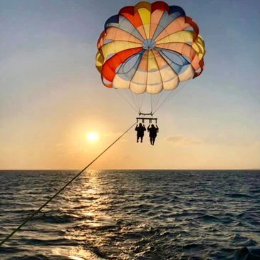 Two people are parasailing over the ocean at sunset.