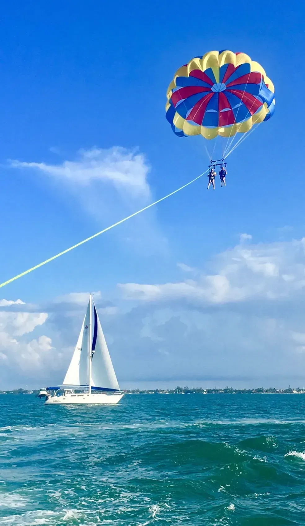 A person is parasailing over a sailboat in the ocean.