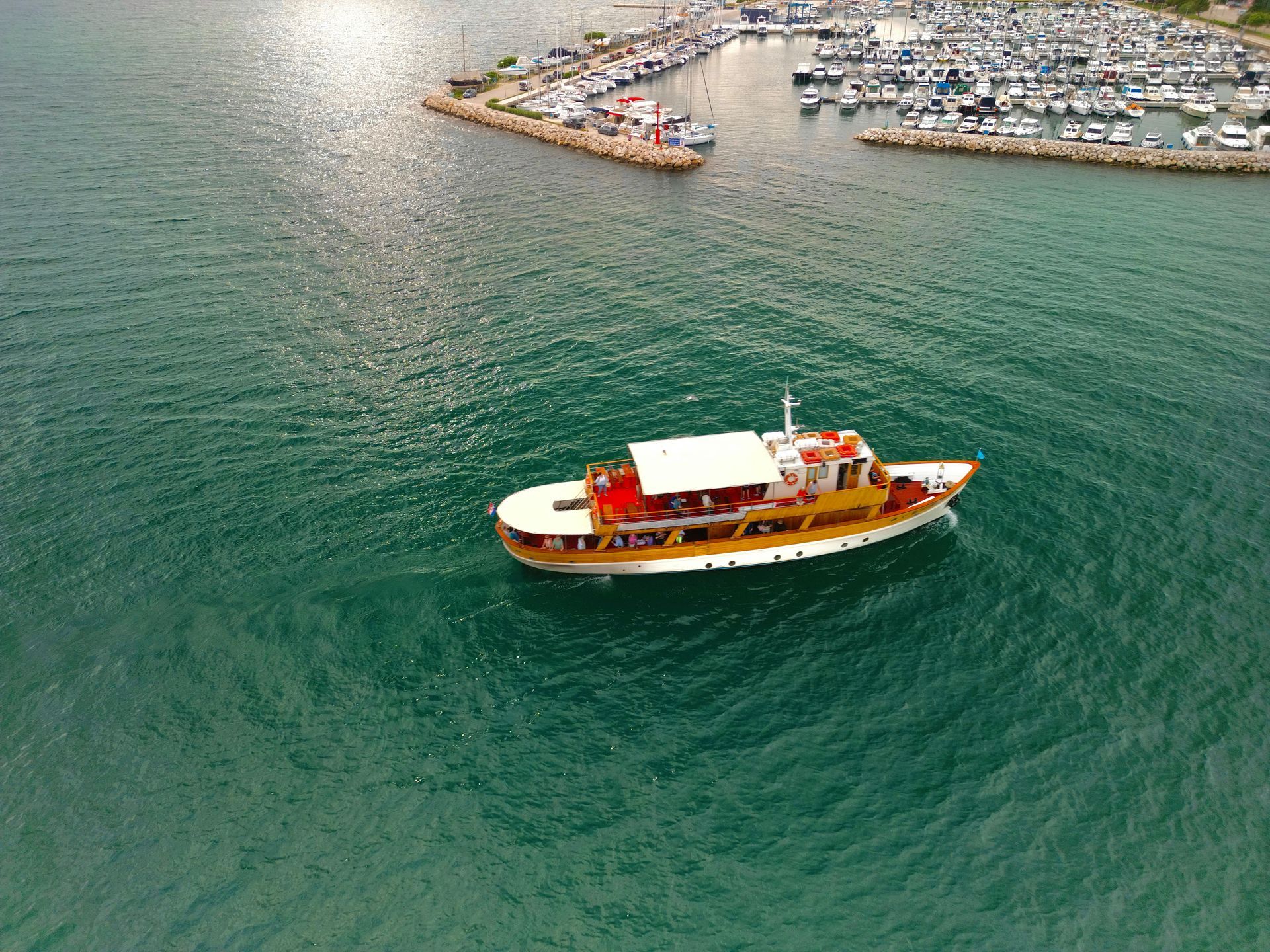 Yellow tour boat sailing on teal water near a marina with many white boats.