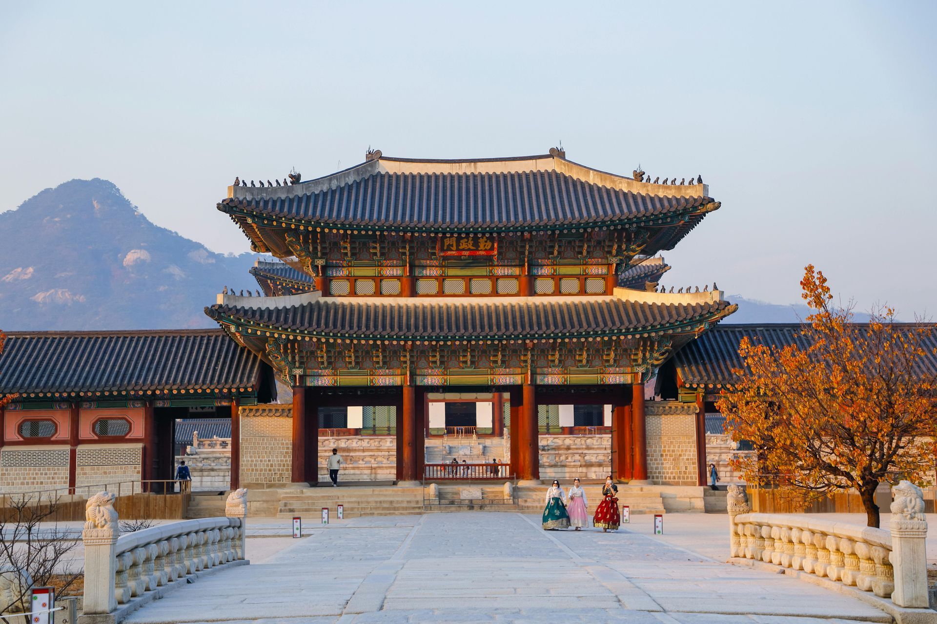 Korean palace gate with snow-covered courtyard; figures in traditional dress.