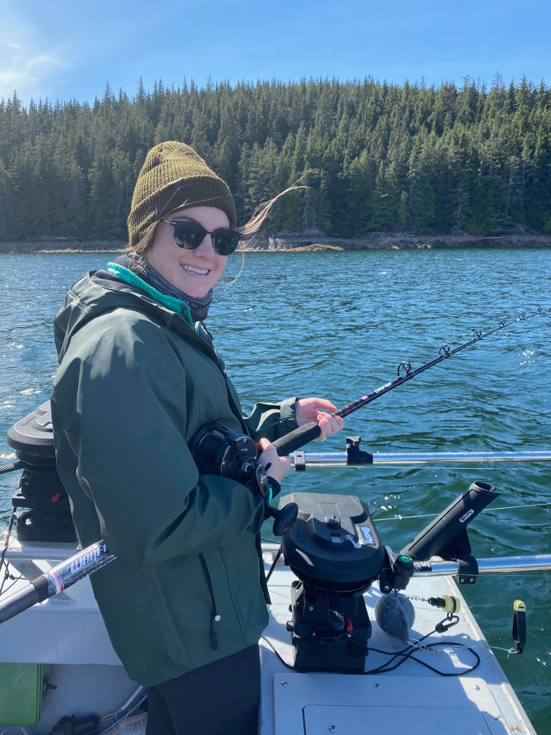 Man fishing from a small boat on calm water; rod bent with a catch.