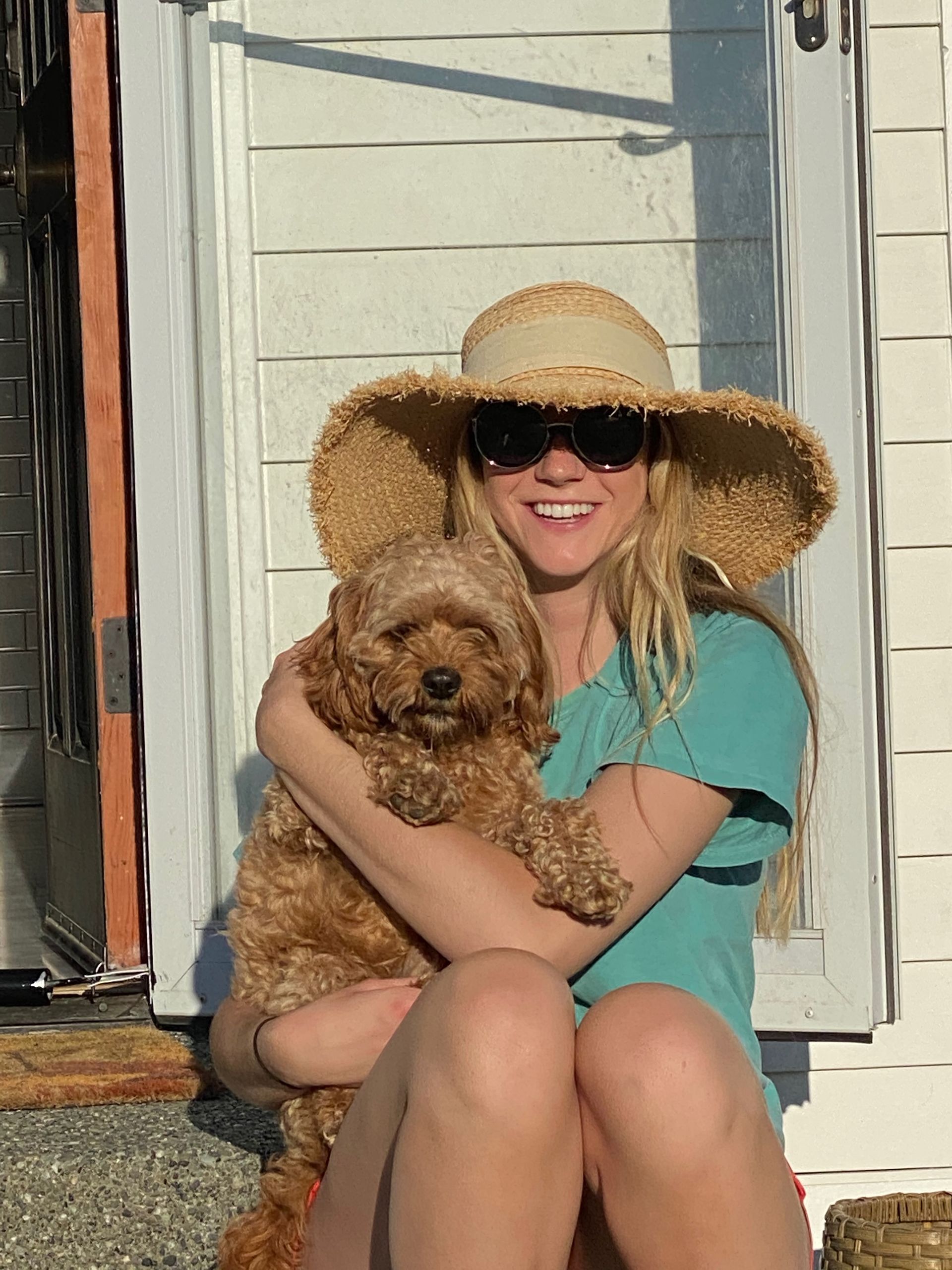 Chef preparing food in a bright kitchen with ocean view, surrounded by ingredients like tomatoes, greens, and pasta.