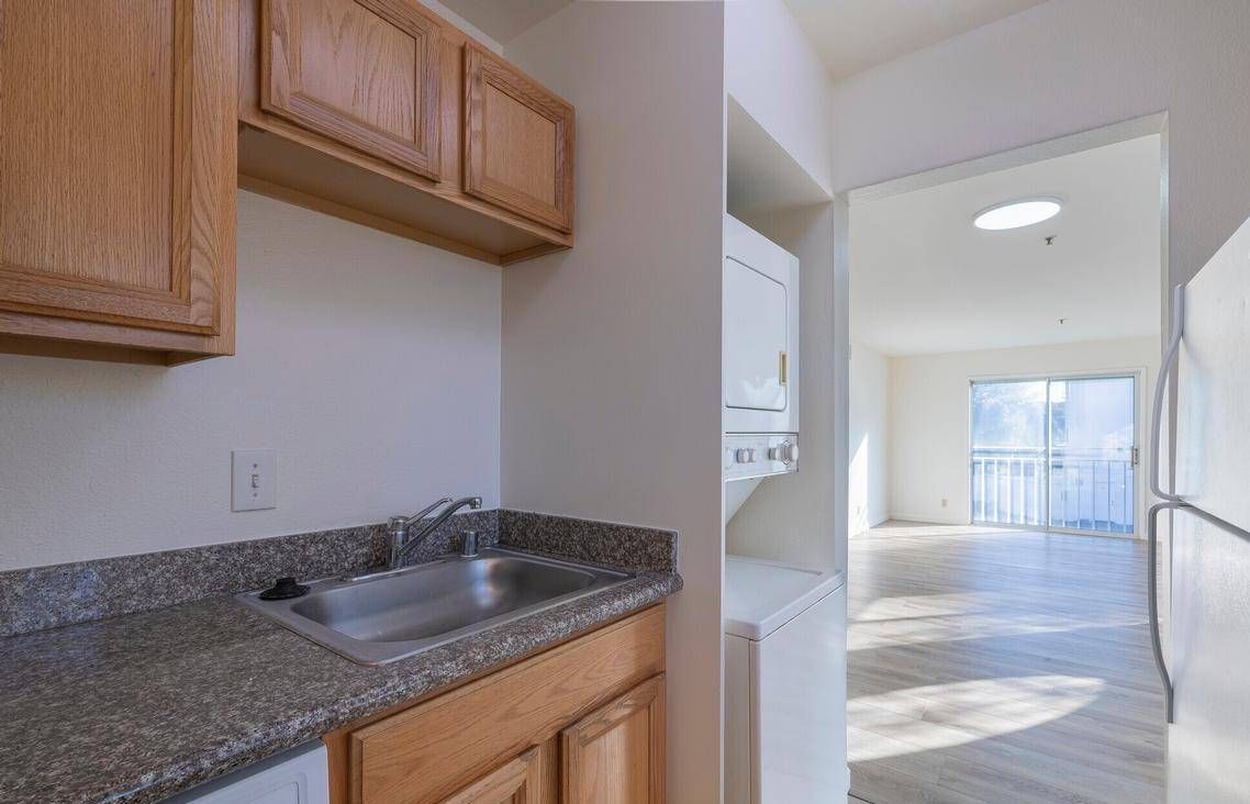 Photo showing a kitchen sink, with a wall next to it that has a washer and dryer on the other side