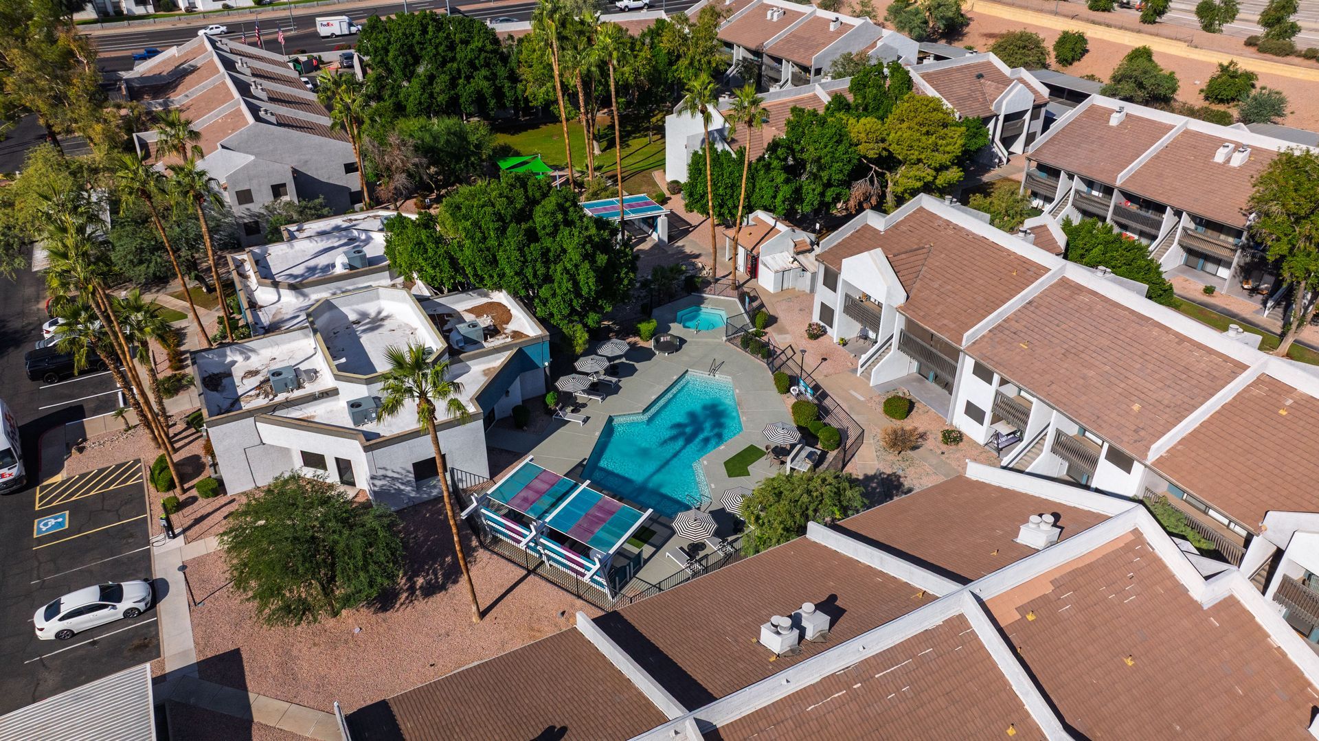 Aerial view of a complex with a pool, buildings with brown roofs, and a parking lot.