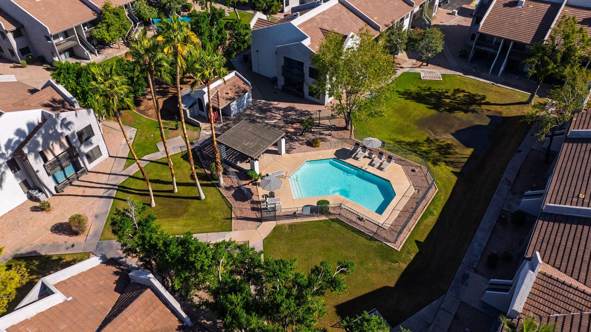 Aerial view of a swimming pool surrounded by a green lawn and buildings with brown roofs.