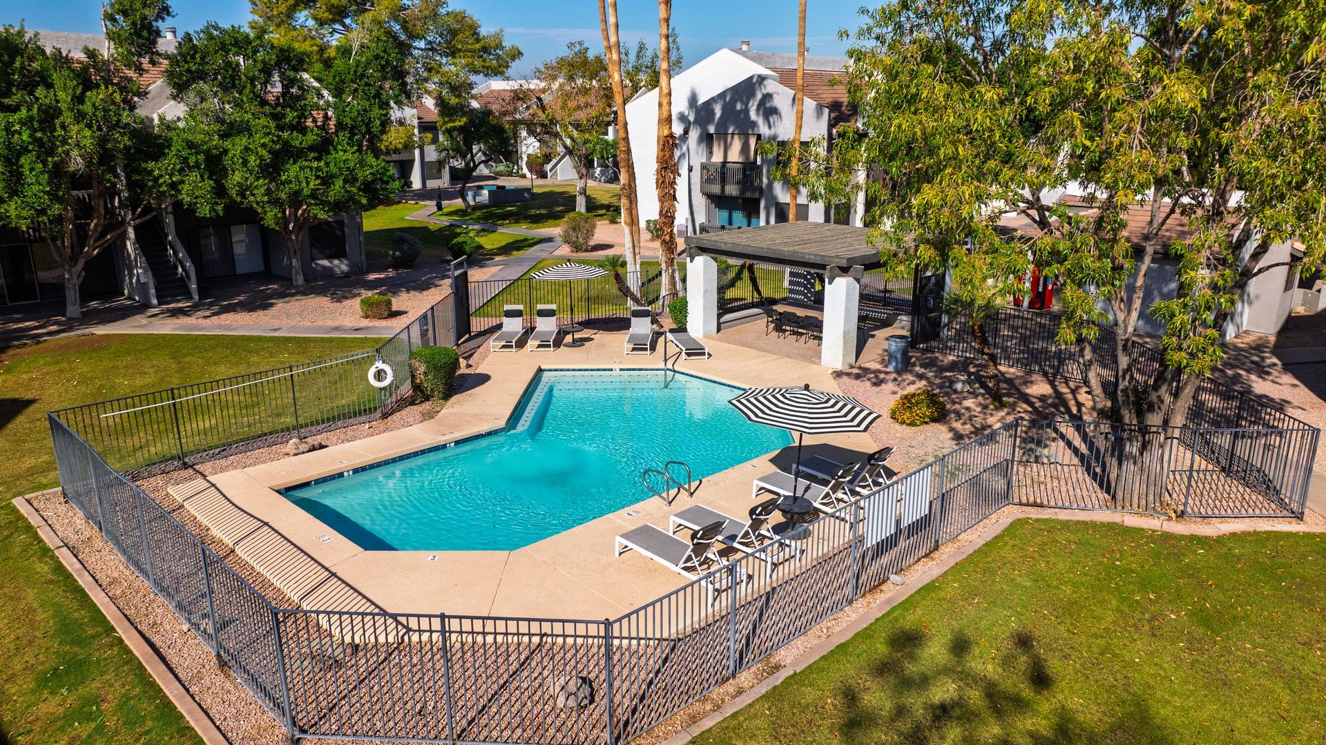 Pool area with a fence, trees, and lounge chairs.