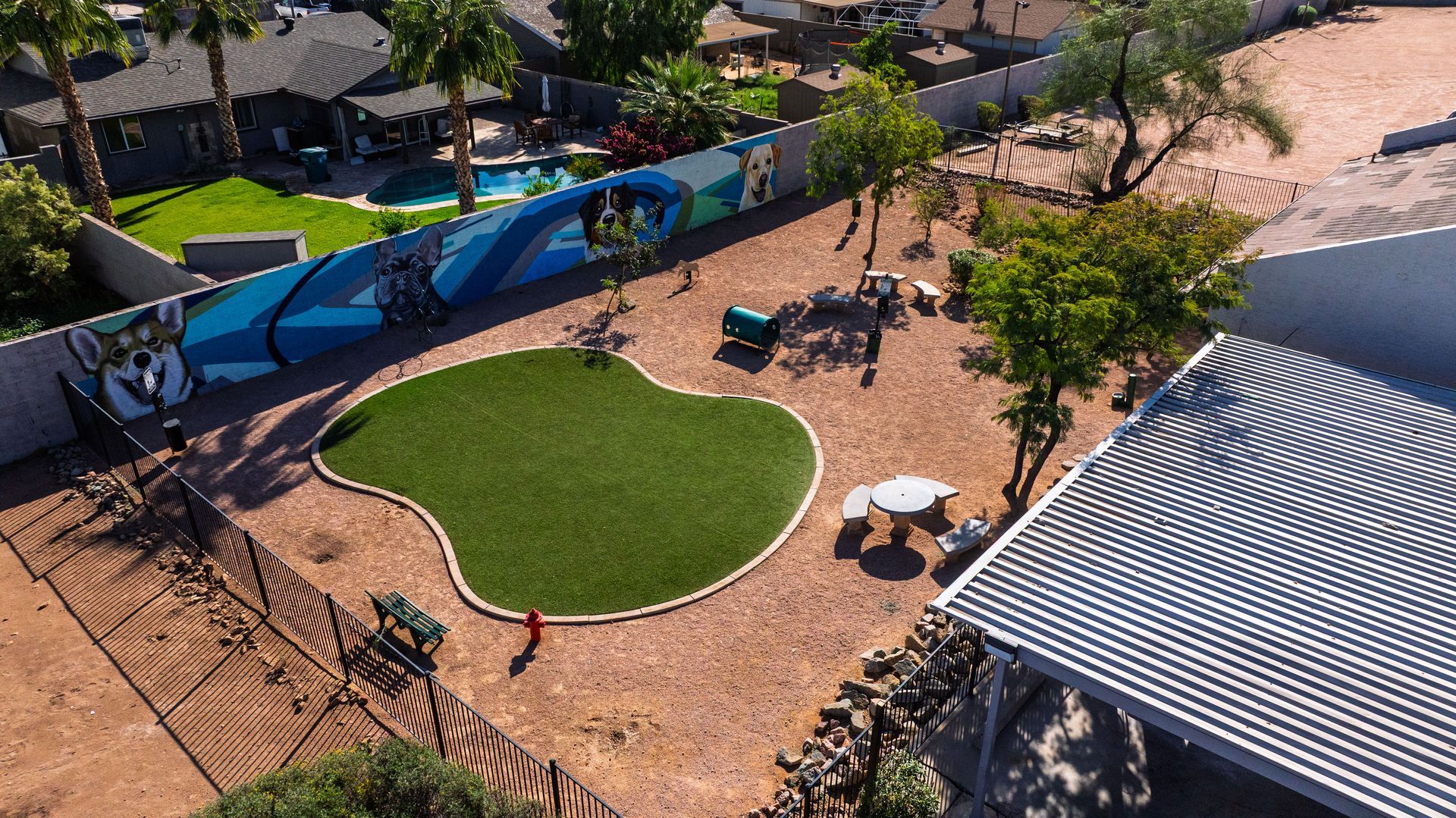 An overhead view of a dog park with artificial turf, red gravel, and a mural.