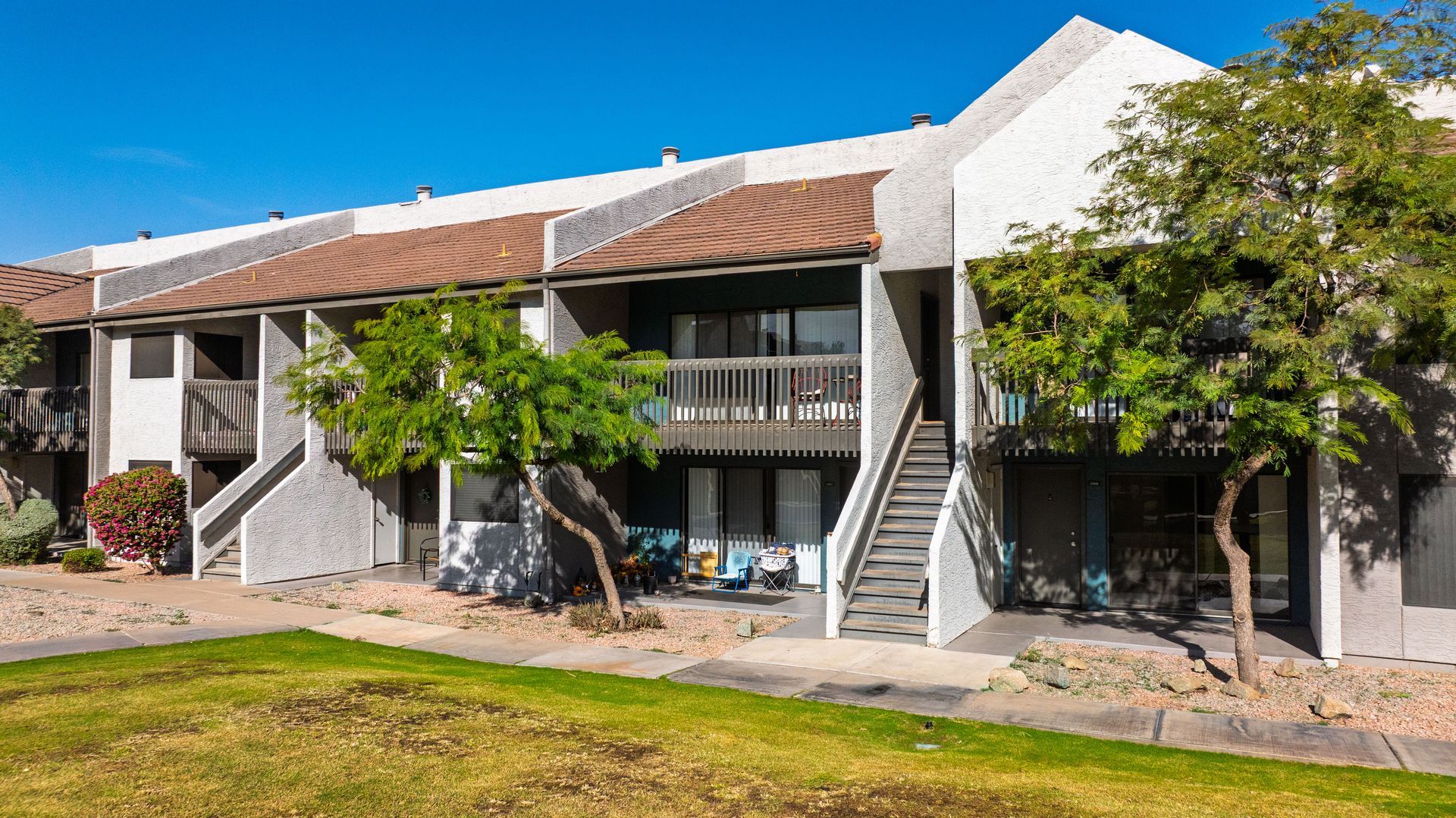 Apartment complex with stucco walls, brown roof, and trees under a clear blue sky.
