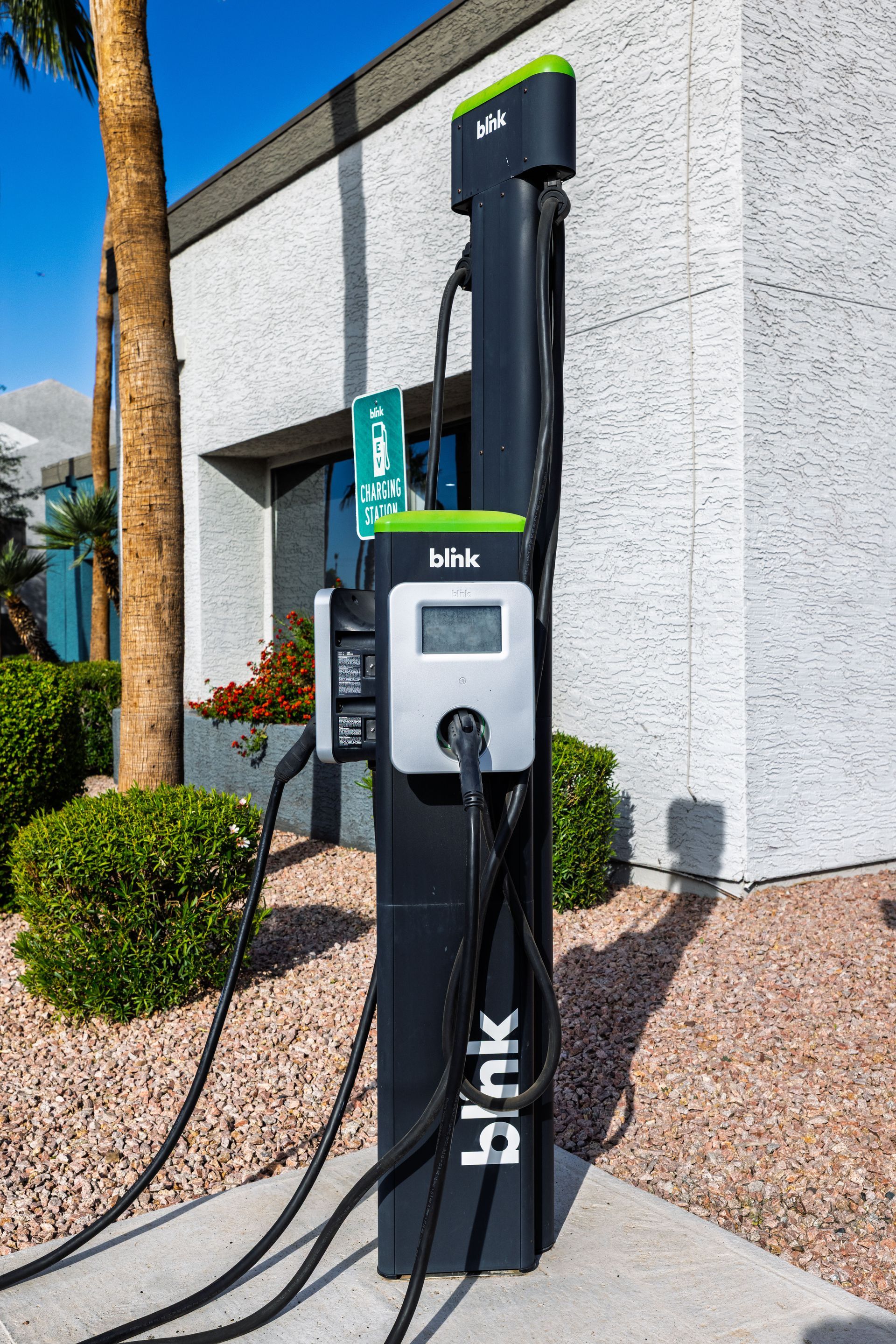Black Blink EV charging station with a screen and cables against a building.