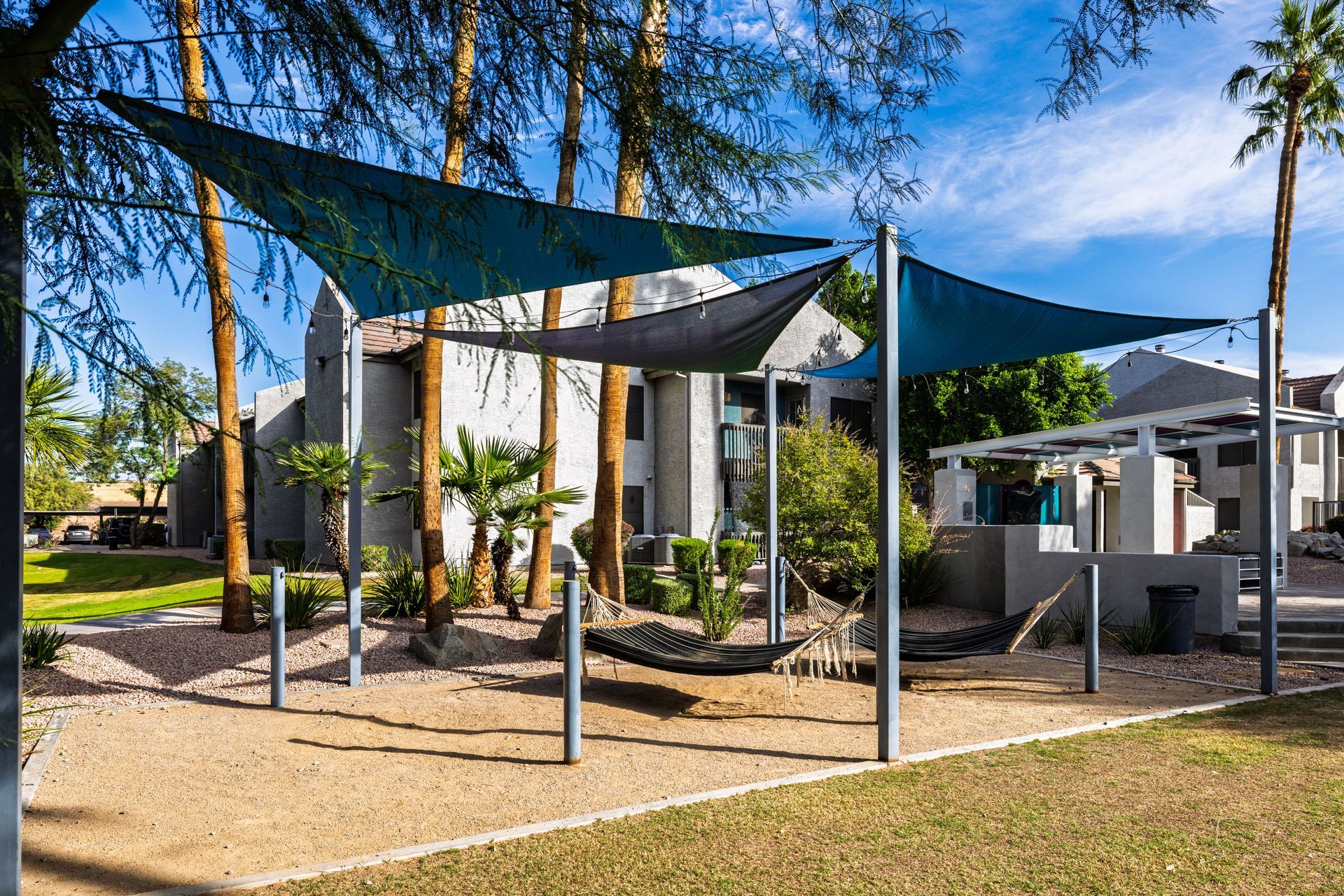 Shade structure with blue canopies over a sand area with a building backdrop.