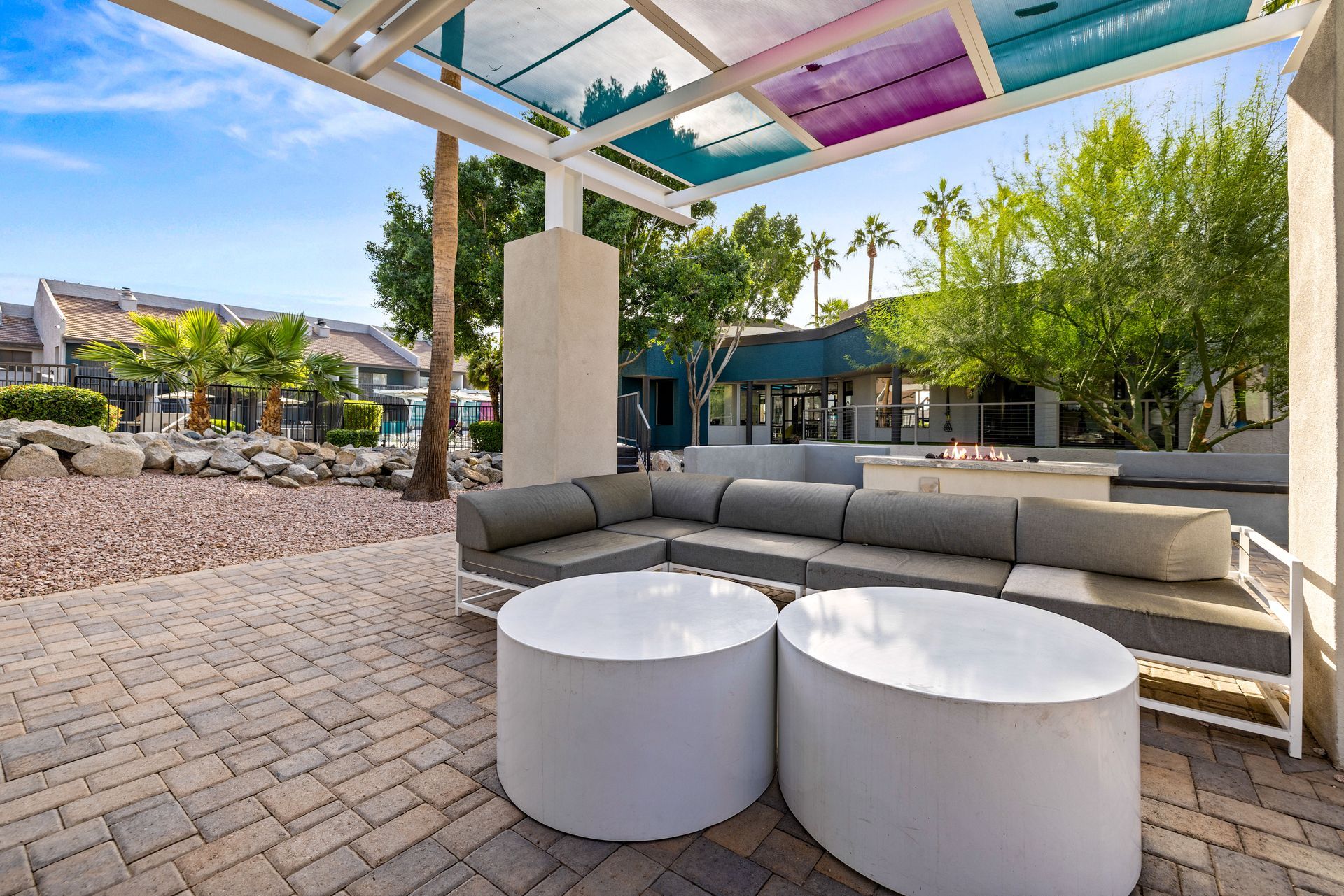 Outdoor patio with seating, white tables, and colorful overhead panels.