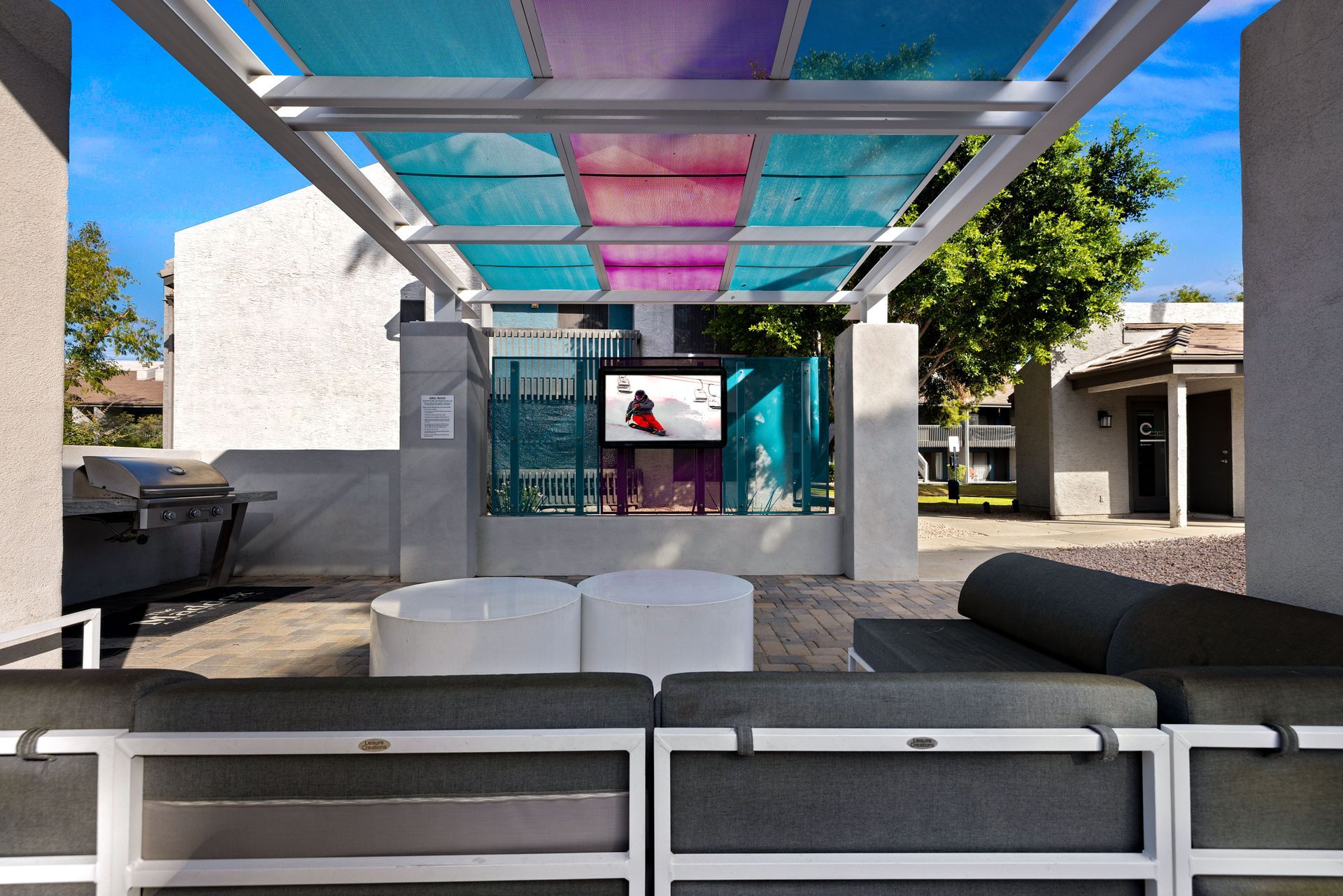Outdoor patio with couch, TV, grill, and colorful shade canopy.