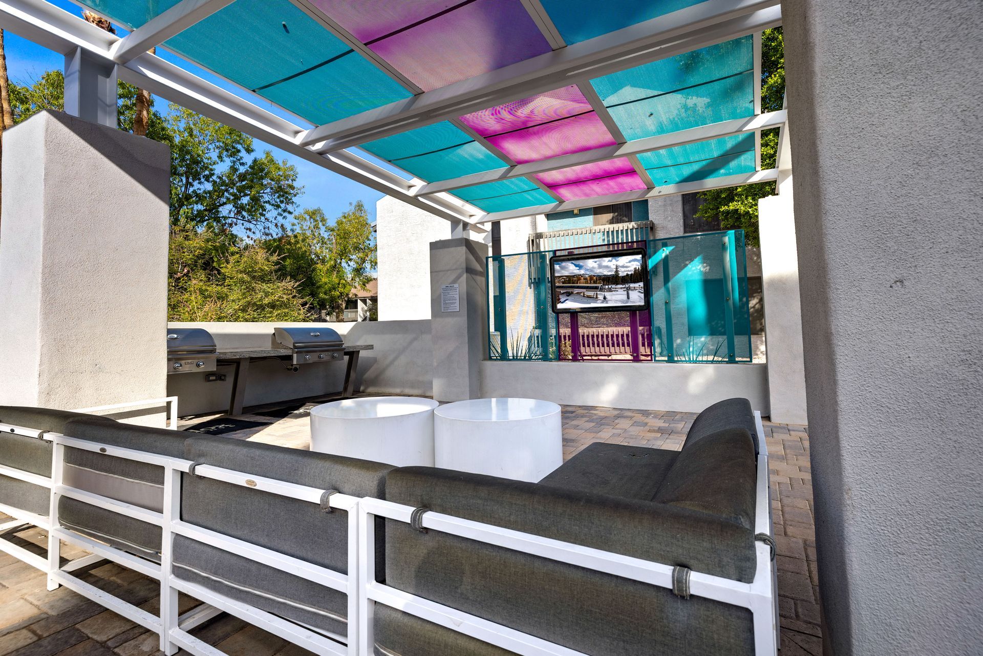 Outdoor patio with grey sofa, grills, and a colorful canopy.