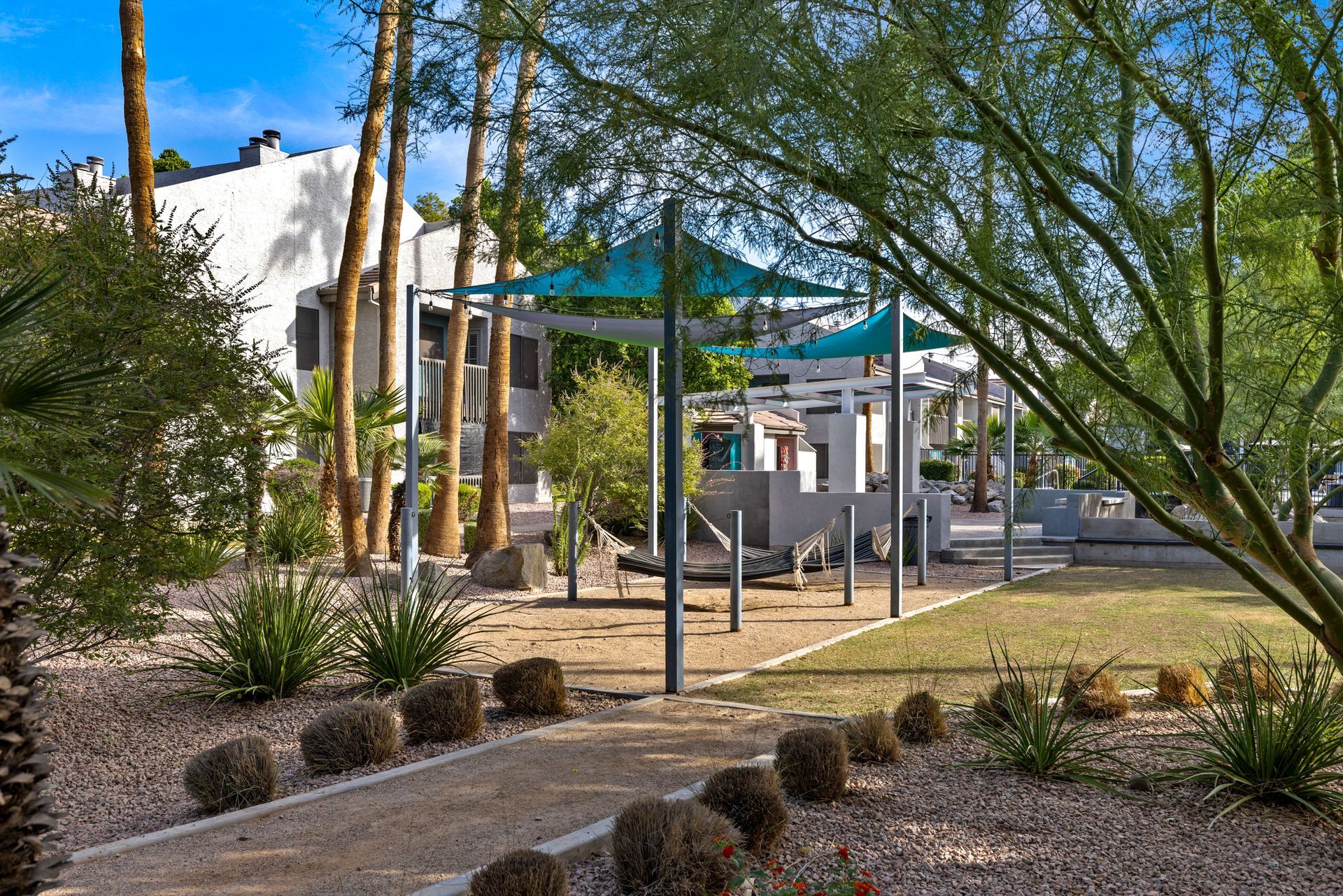 Desert landscaping with gravel path, shade structures, and light-colored buildings in background.