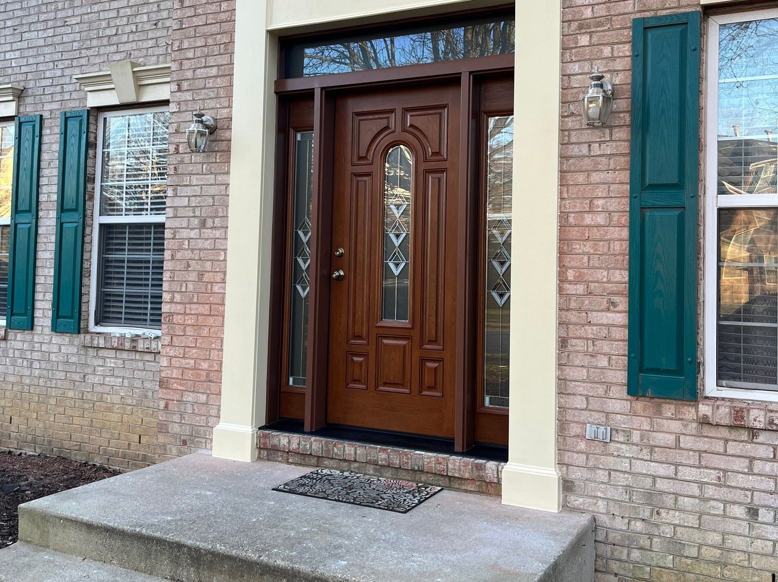 The front door of a brick house with a wooden door and green shutters.