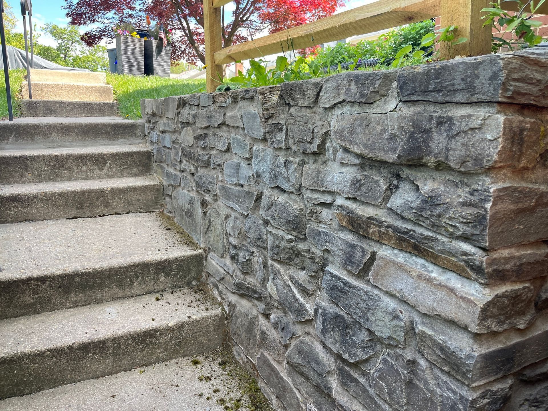 A stone wall surrounds a set of stairs leading up to a house.