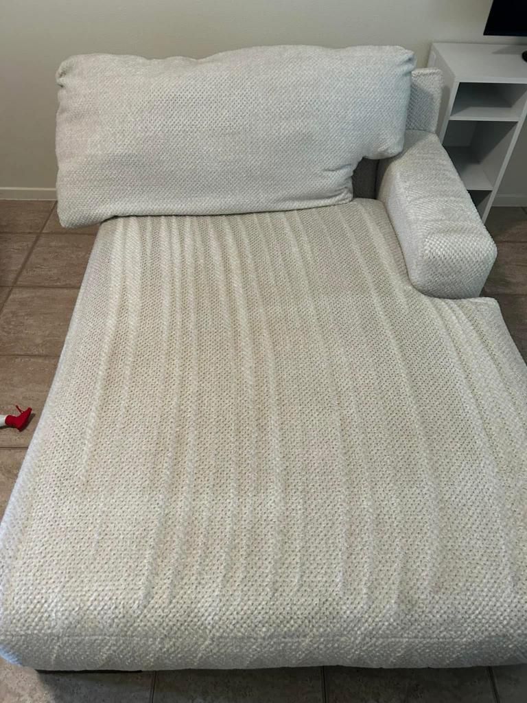 A white couch with two pillows on it is sitting on a tiled floor in a living room.