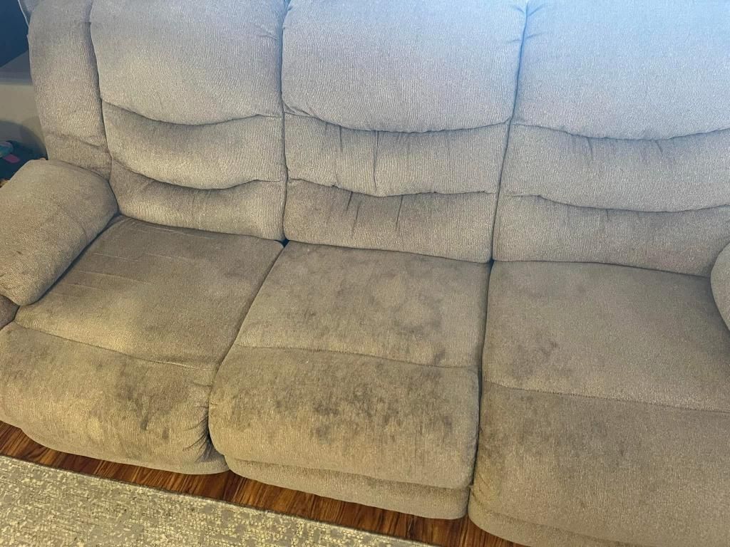 A beige couch is sitting on a wooden floor in a living room.