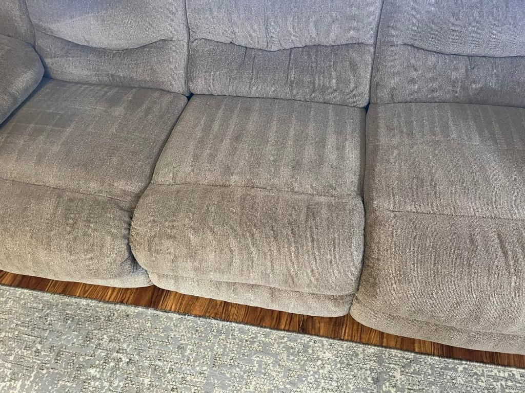 A couch is sitting on a wooden floor next to a rug.