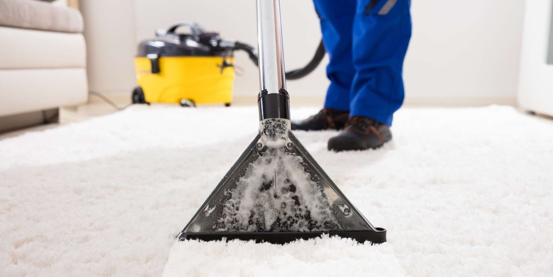 A man is cleaning a carpet with a vacuum cleaner.