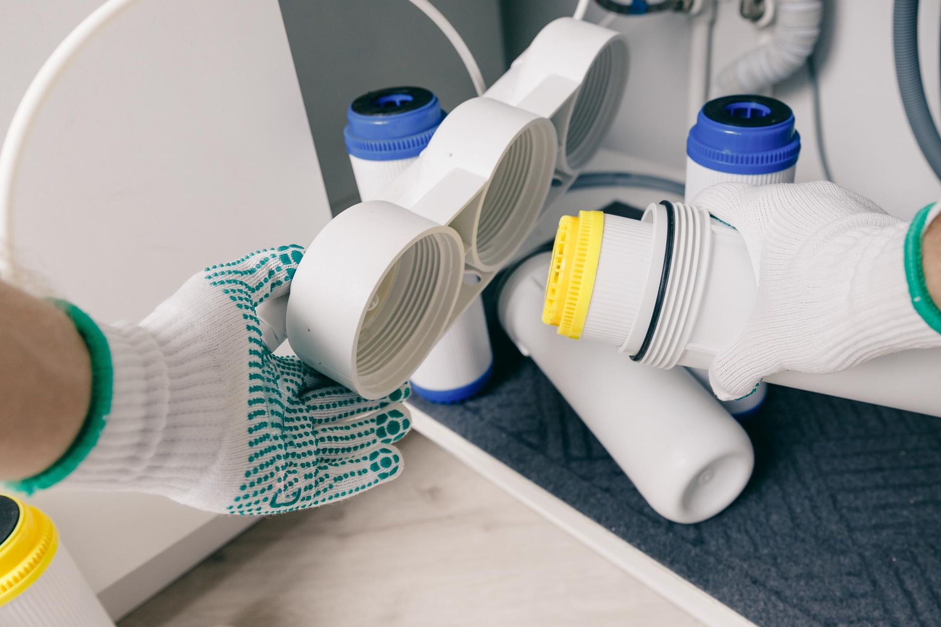 Hands in gloves assembling water filter parts under a sink.