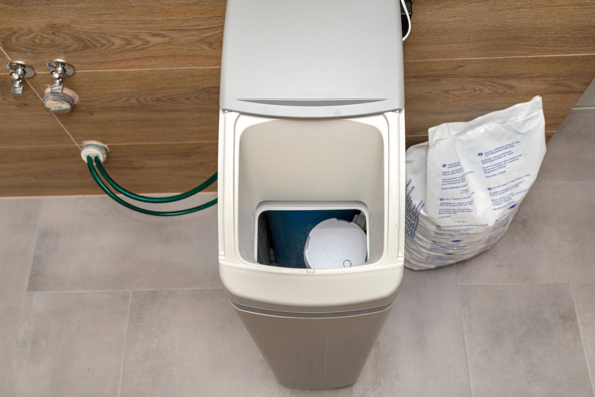 Top-down view of a wall-mounted toilet with the tank open. A bag of white powder sits beside it.