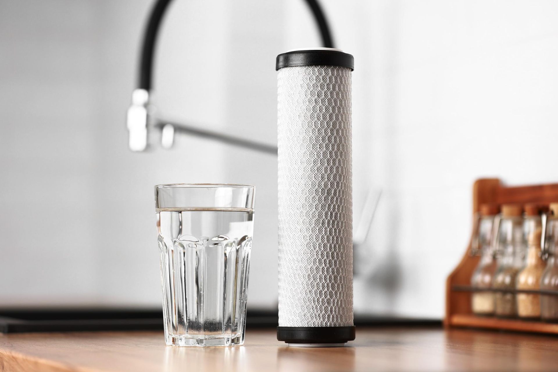 A glass of water and a water filter next to a kitchen faucet.