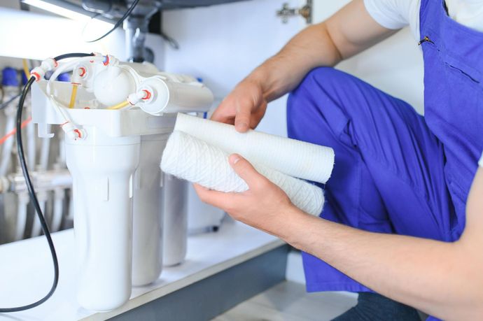 A person in blue overalls replacing water filters under a sink. 