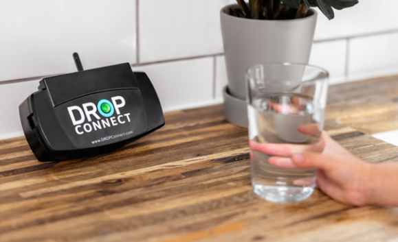 Black Drop Connect device on a wooden countertop with a child's hand reaching for a glass of water.