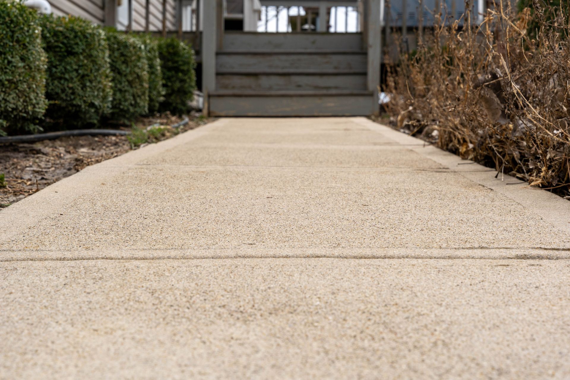 A concrete walkway leading to a house with stairs.