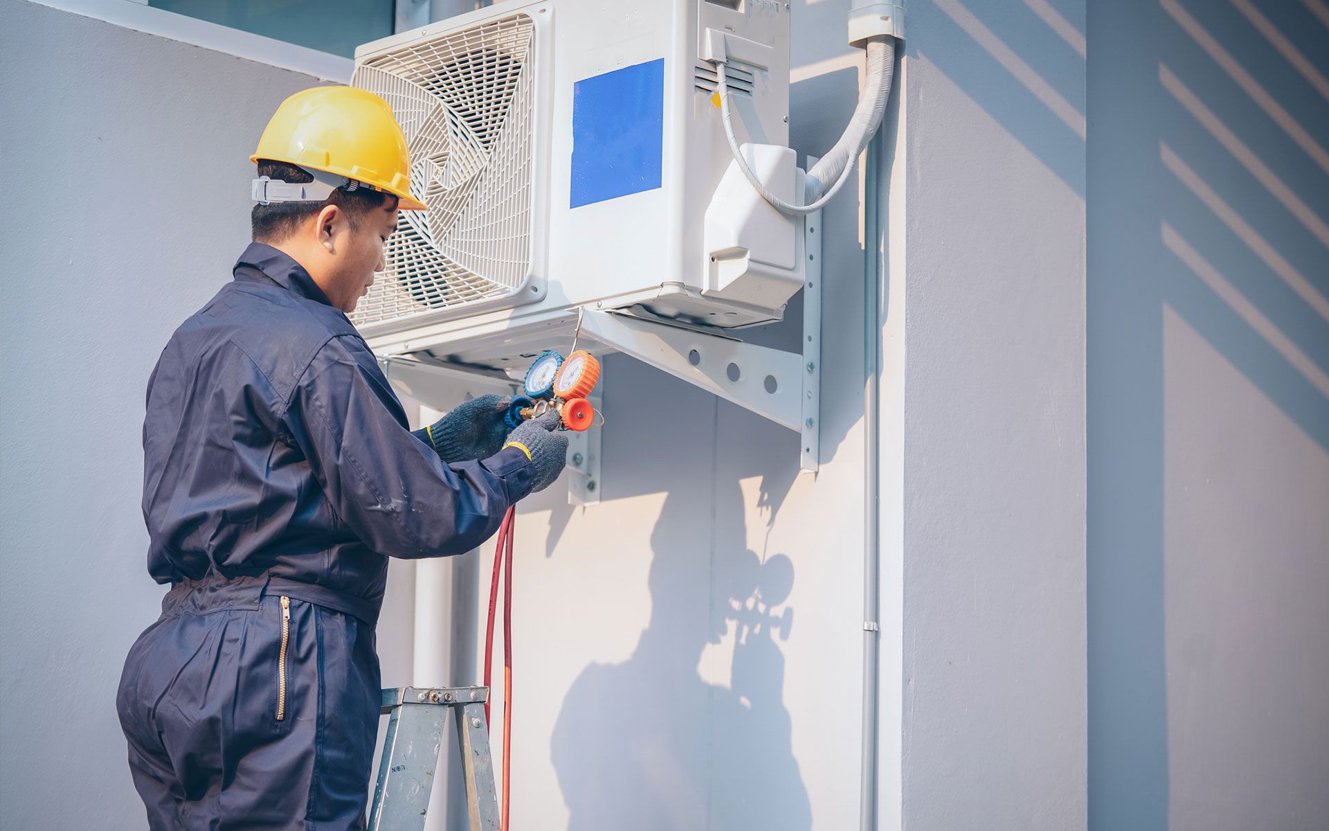 A man is working on an air conditioner on the side of a building.