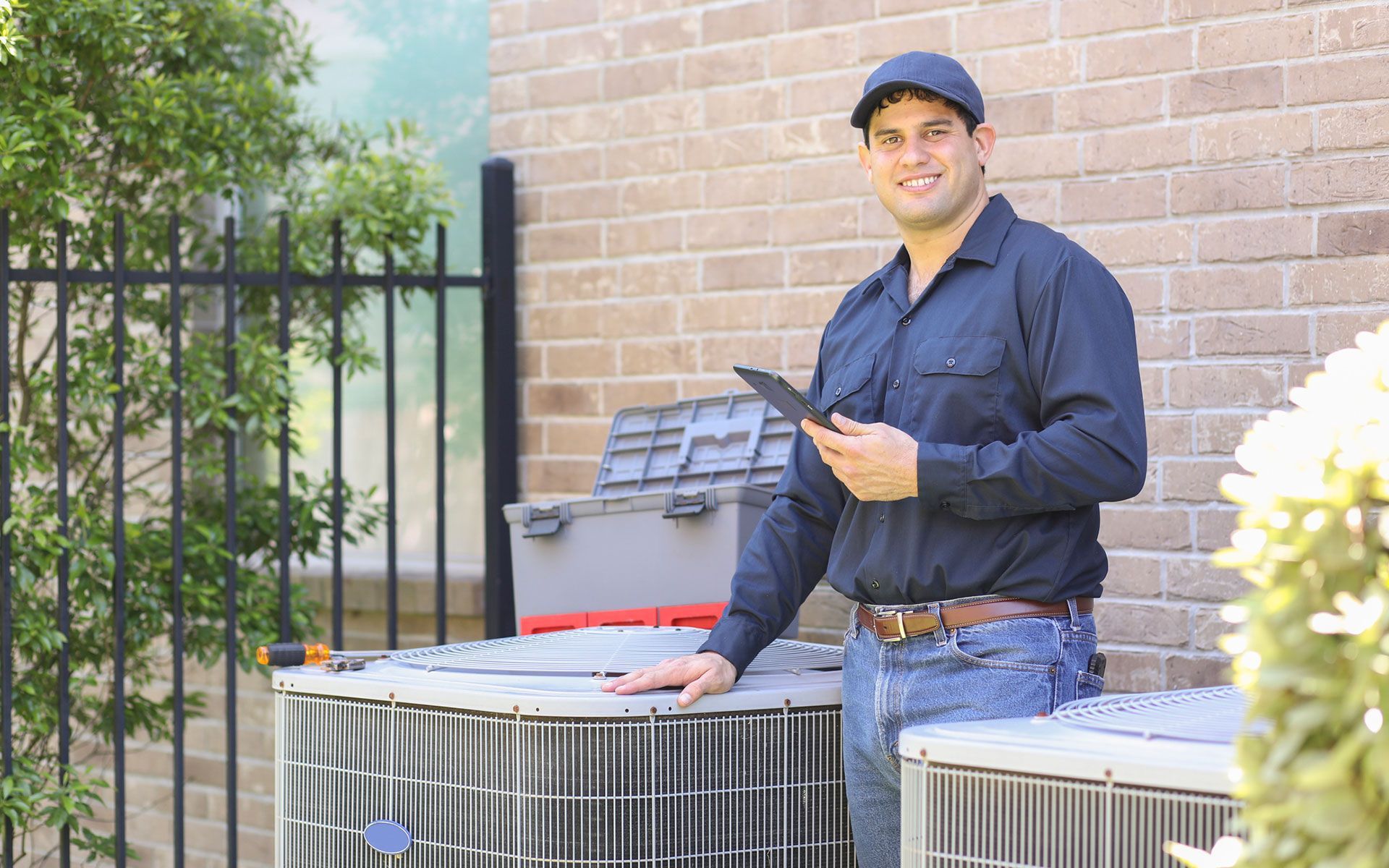 A man is standing in front of a brick building holding a tablet.