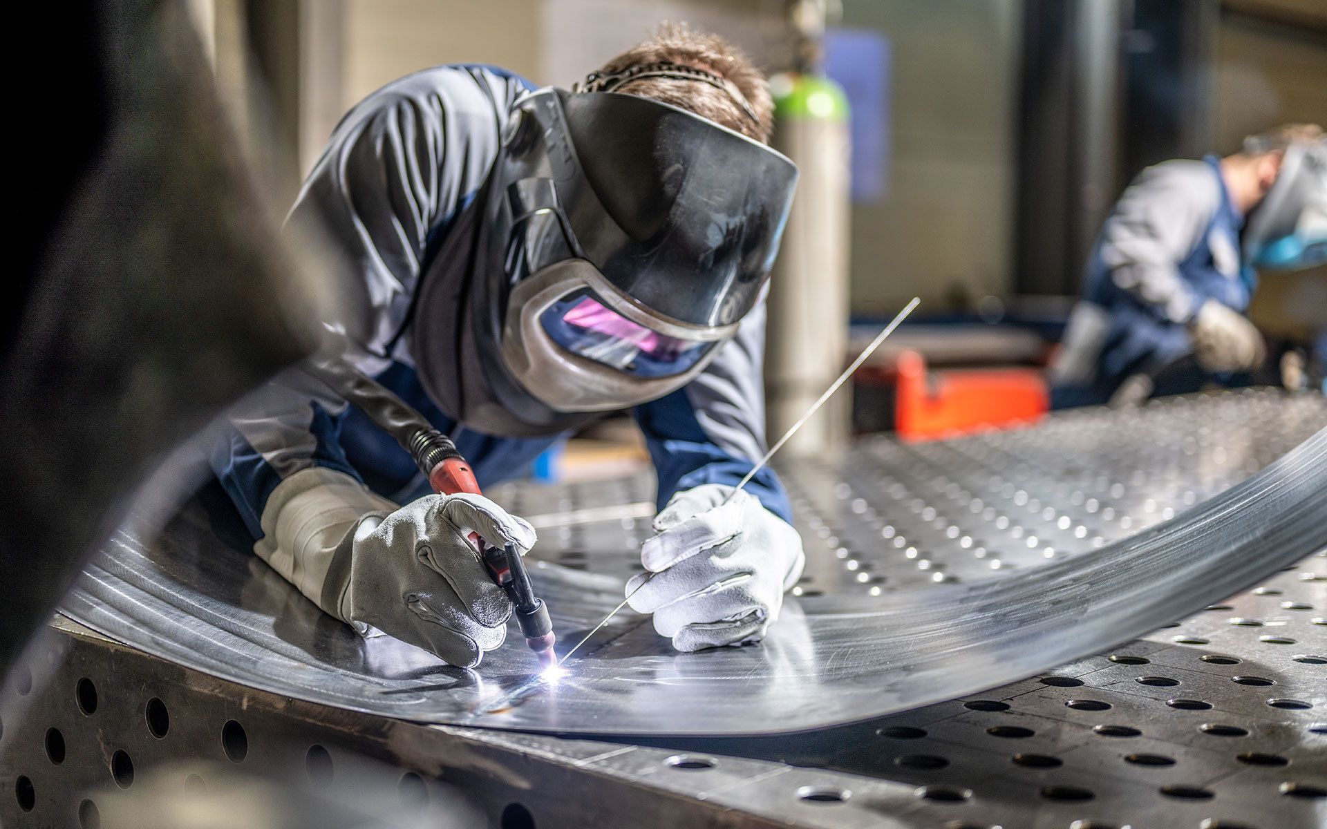 A man is welding a piece of metal in a factory.