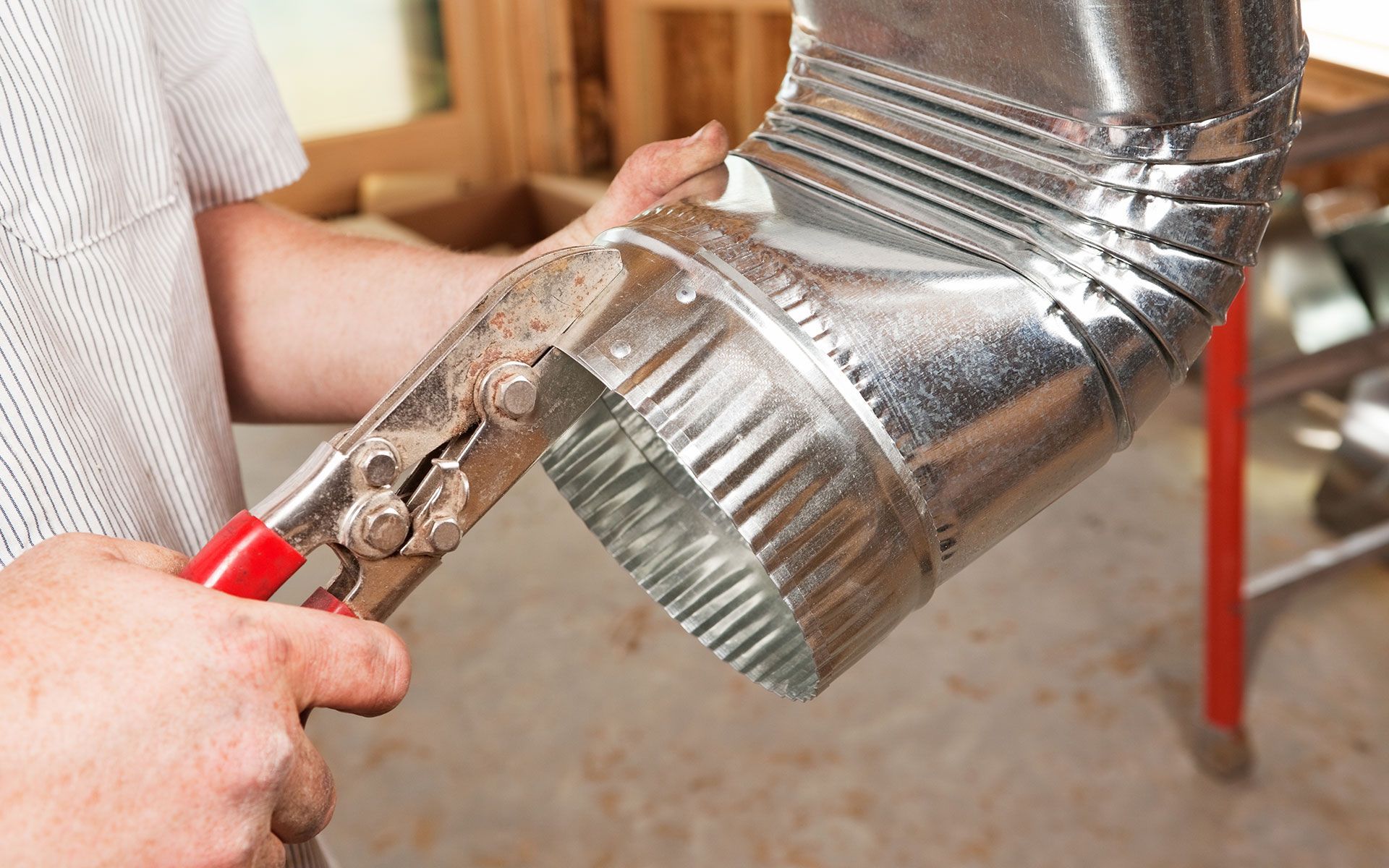 A person is holding a pair of pliers over a metal pipe.