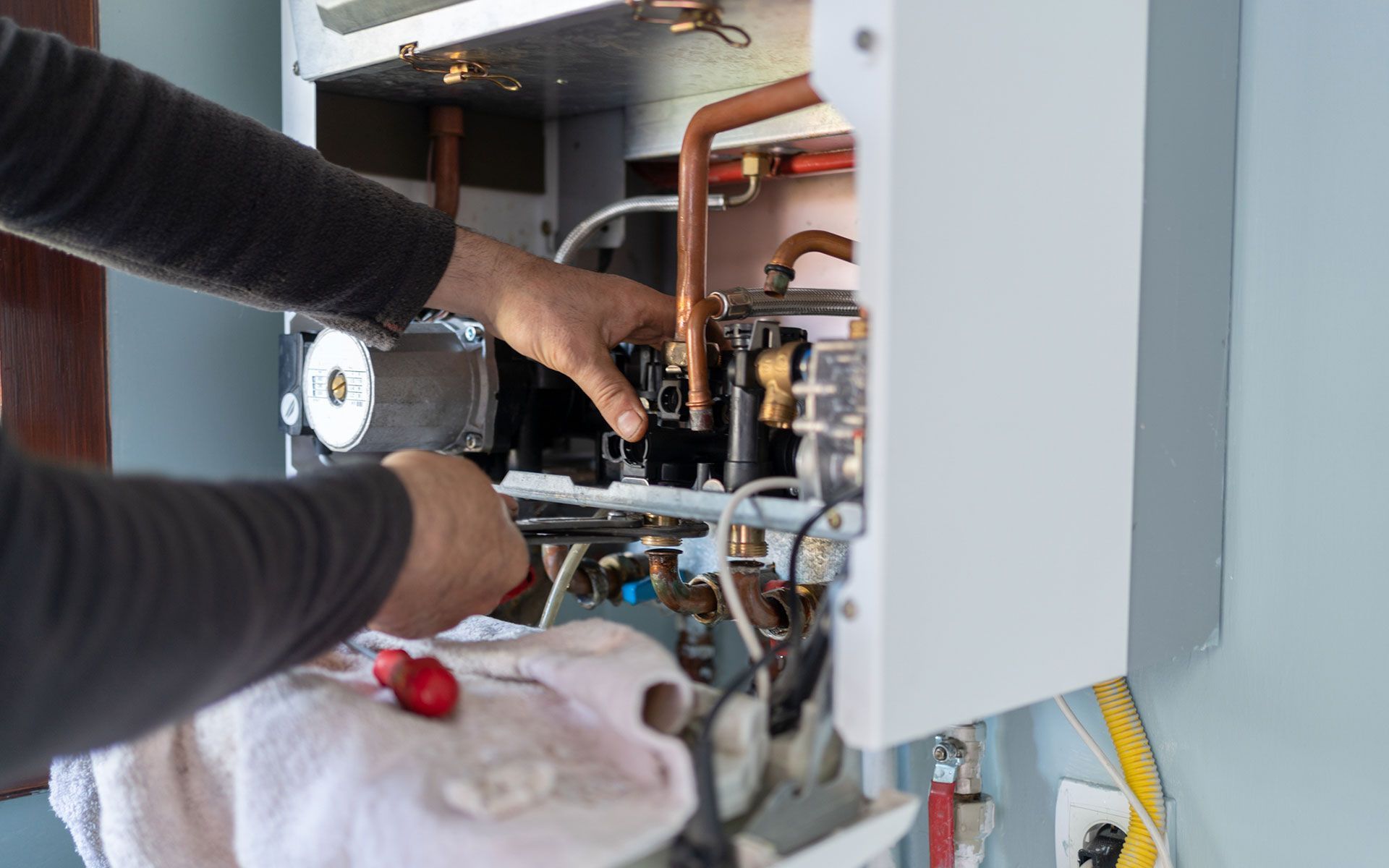 A man is fixing a boiler with a wrench and a towel.
