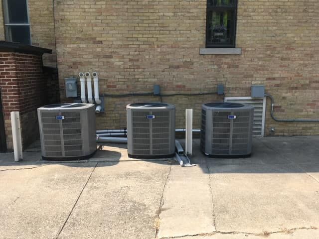 Three air conditioners are sitting outside of a brick building.
