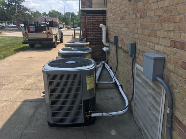 A row of air conditioners are sitting on the side of a brick building.