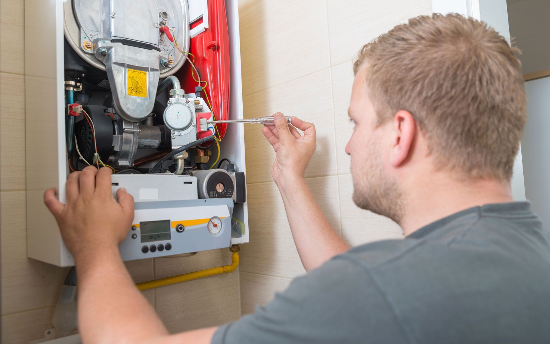 A man is fixing a boiler with a screwdriver.