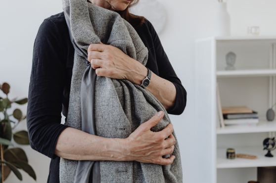 A person in a black long-sleeved shirt holds a folded gray wool coat against their chest in a bright, modern room.