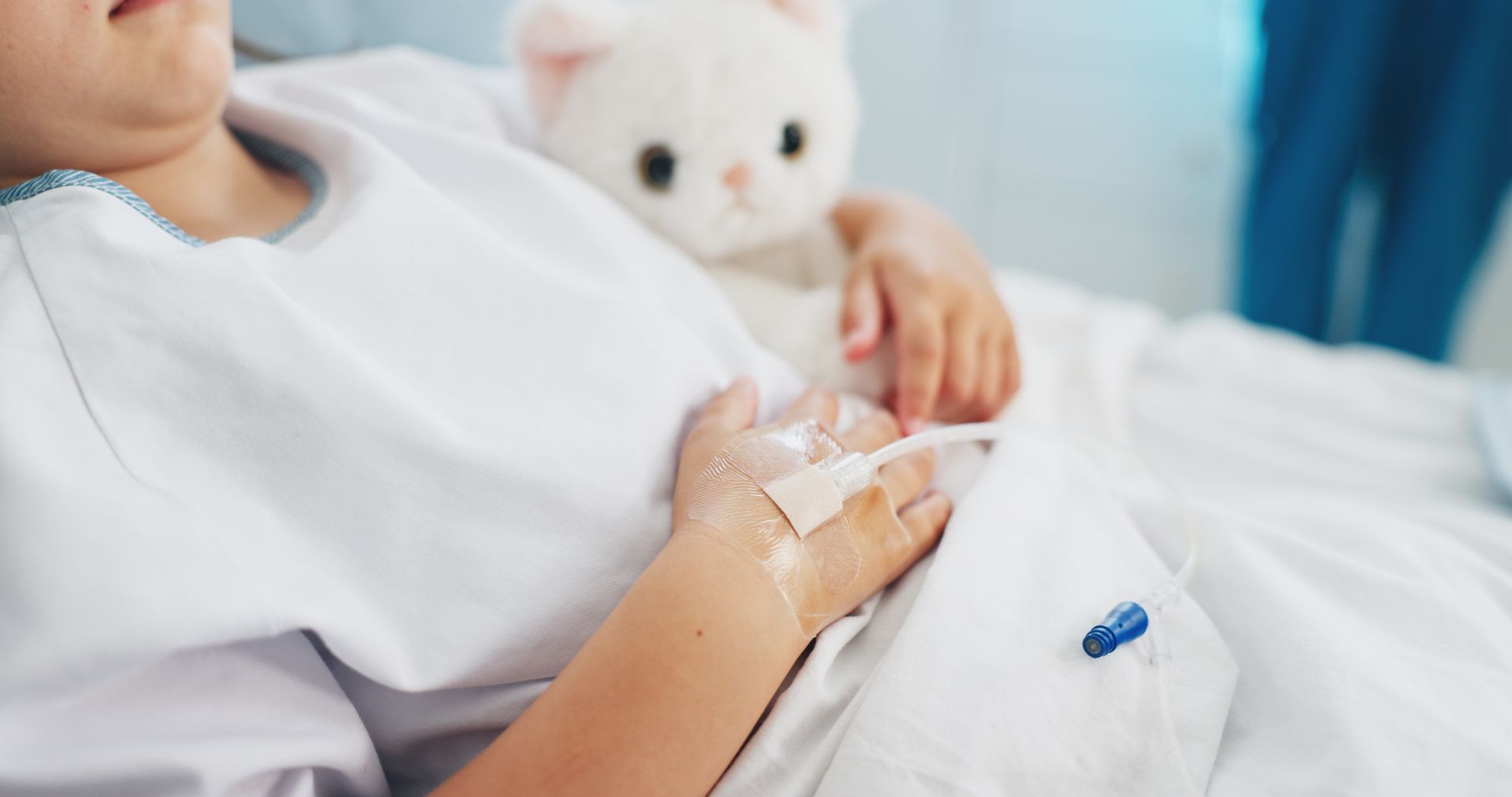 Patient resting in a hospital bed holding a stuffed bear, with an IV in the hand