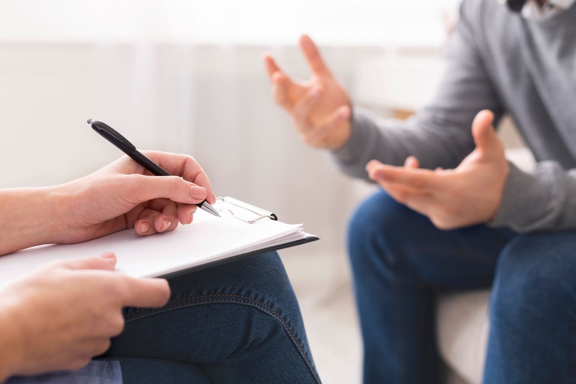 Person writing on clipboard, listening to another person gesturing with hands.