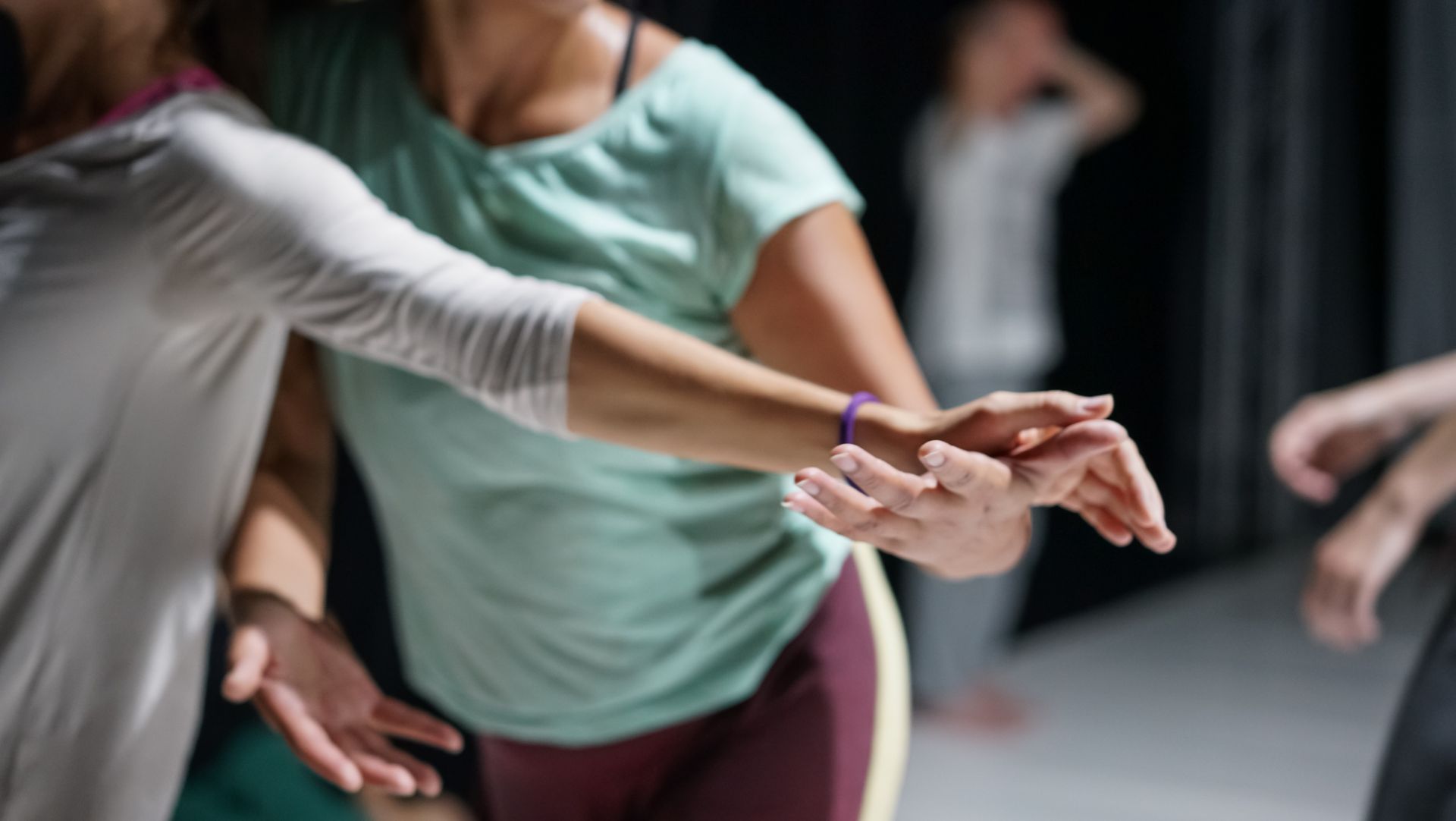 Two people in a dance studio practice a movement, reaching toward each other with their hands.