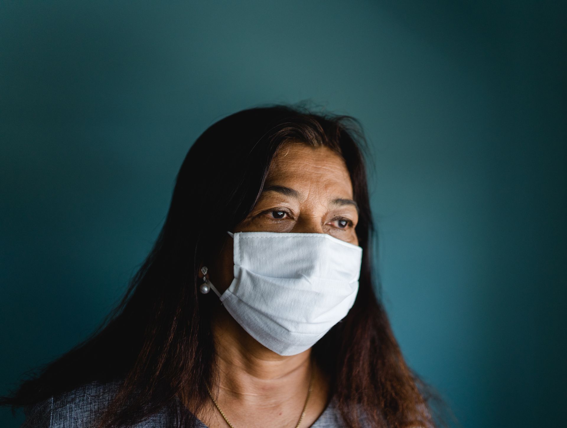 Person wearing a white face mask against a dark teal background