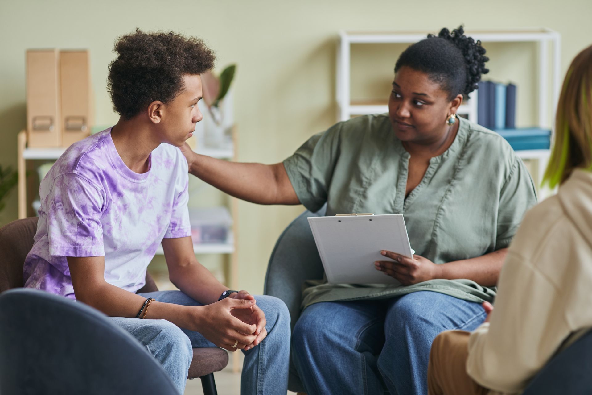 Therapist comforting a person in a support group. Hand on shoulder, holding clipboard.
